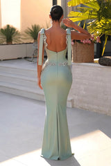 Woman in a light green evening gown with floral details standing on a rooftop.
